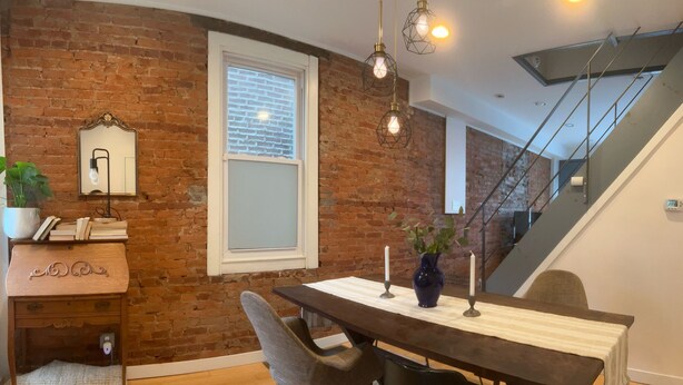 A dining area with a brick wall, a wooden table, and chairs. There is a staircase in the background.