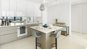 A modern kitchen with white cabinetry, a central island with bar stools, and pendant lighting. - A1302 (Cupecoy)