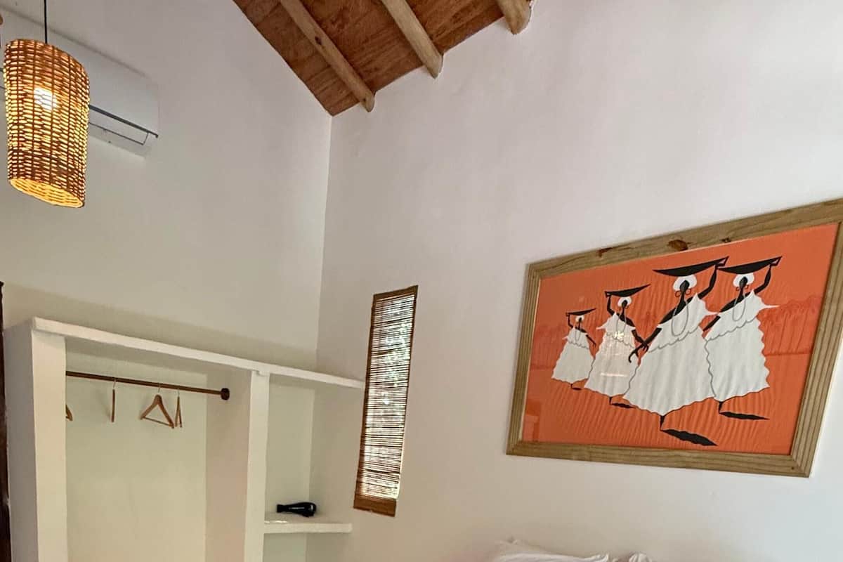 A bedroom with a large bed, a wooden ceiling, a hanging light fixture, a towel on the bed, a mirror, and a painting on the wall.
