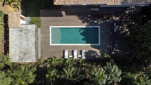 Ein Blick von oben auf einen Poolbereich mit einem rechteckigen Pool, umgeben von einer Holzterrasse und Liegestühlen.