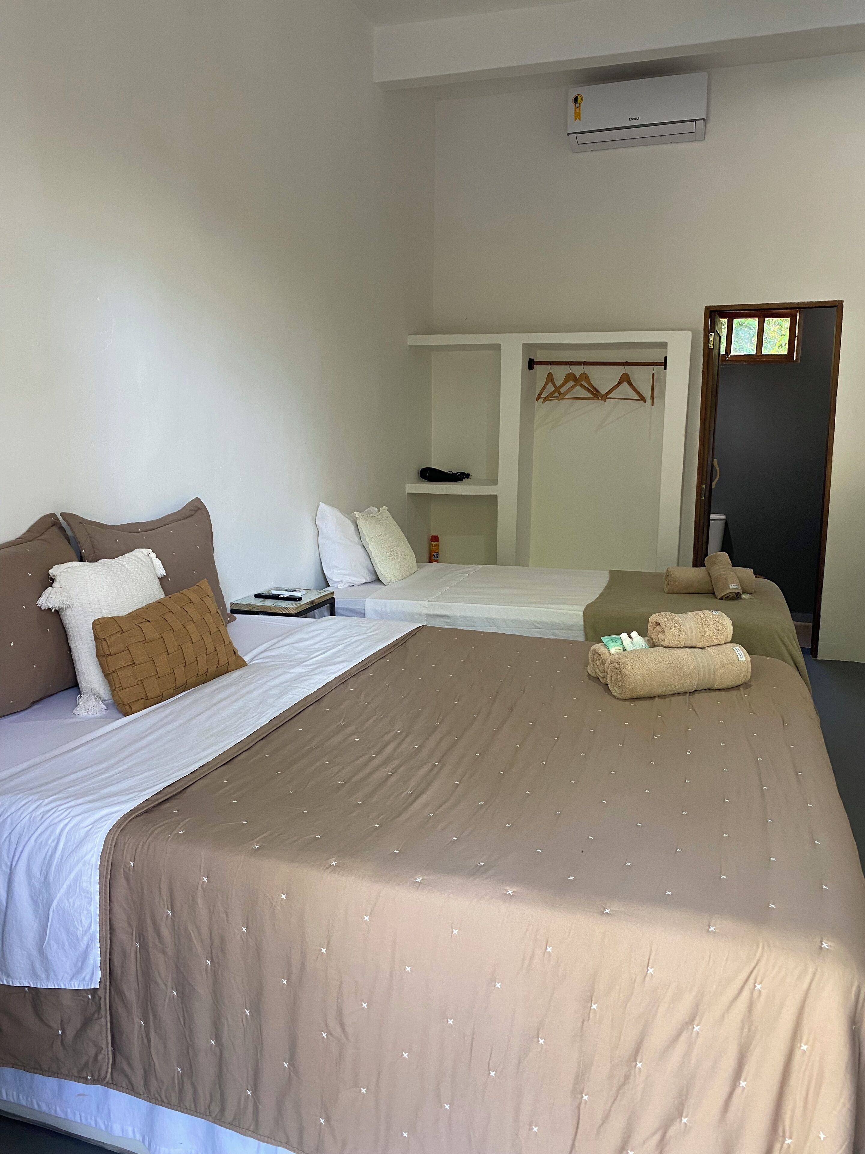 Une chambre d’hôtel avec deux lits, une armoire, une petite table et un appareil de climatisation.