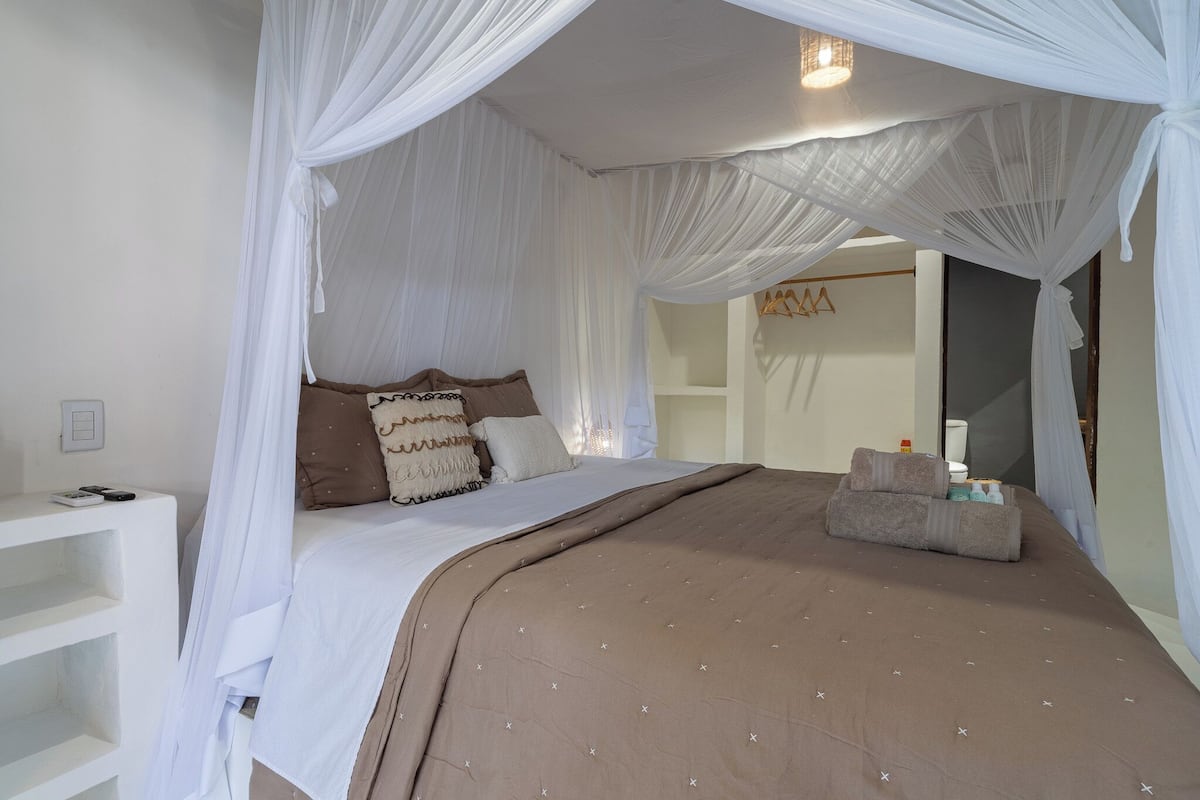 A neatly arranged bedroom with a bed, white curtains, and a bedside table.