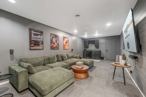 Een moderne woonkamer met een groene modulaire bank, een ronde houten salontafel en een flatscreen televisie aan de muur.