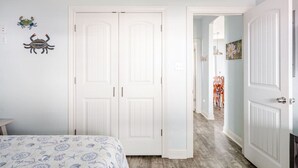 A bedroom with a bed, two white doors, and a hallway leading to a dining area. - Beachfront 3BR/2BA – Steps to the Sand, Huge Deck (Bolivar Peninsula)