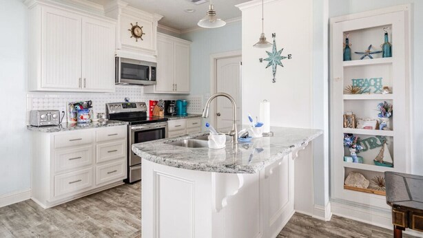 A modern kitchen with white cabinetry, a granite countertop, a built-in microwave, and a coffee maker. - Beachfront 3BR/2BA – Steps to the Sand, Huge Deck (Bolivar Peninsula)