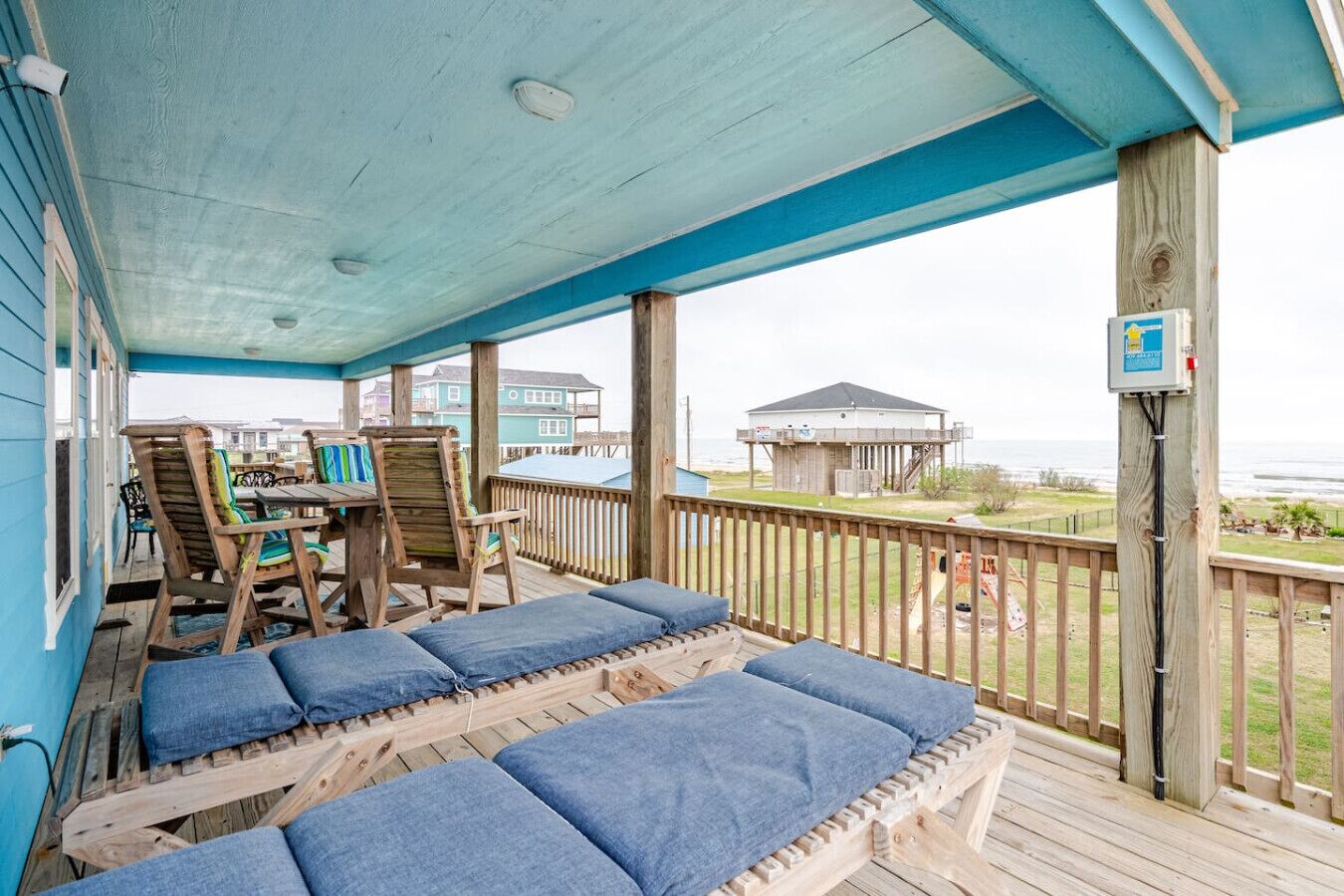 Un espace extérieur abrité, doté de bancs et de chaises en bois, offrant une vue sur la plage et l’océan.