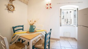 A dining area with a table, chairs, a vase with dried flowers, a life preserver decoration, and a view through an open door.
