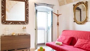 A room with a wooden dresser, a red sofa, two ornate mirrors, and a window with a view.