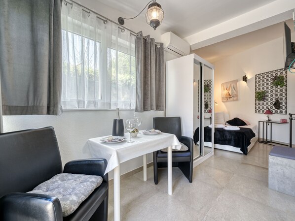 Une chambre d’hôtel moderne avec un coin repas, un lit recouvert d’une couverture noire, une petite table avec une nappe blanche et une chaise.