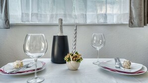 Una mesa de comedor dispuesta con dos platos, dos copas de vino, una botella de vino, un florero decorativo, y un tenedor y un cuchillo en cada plato.