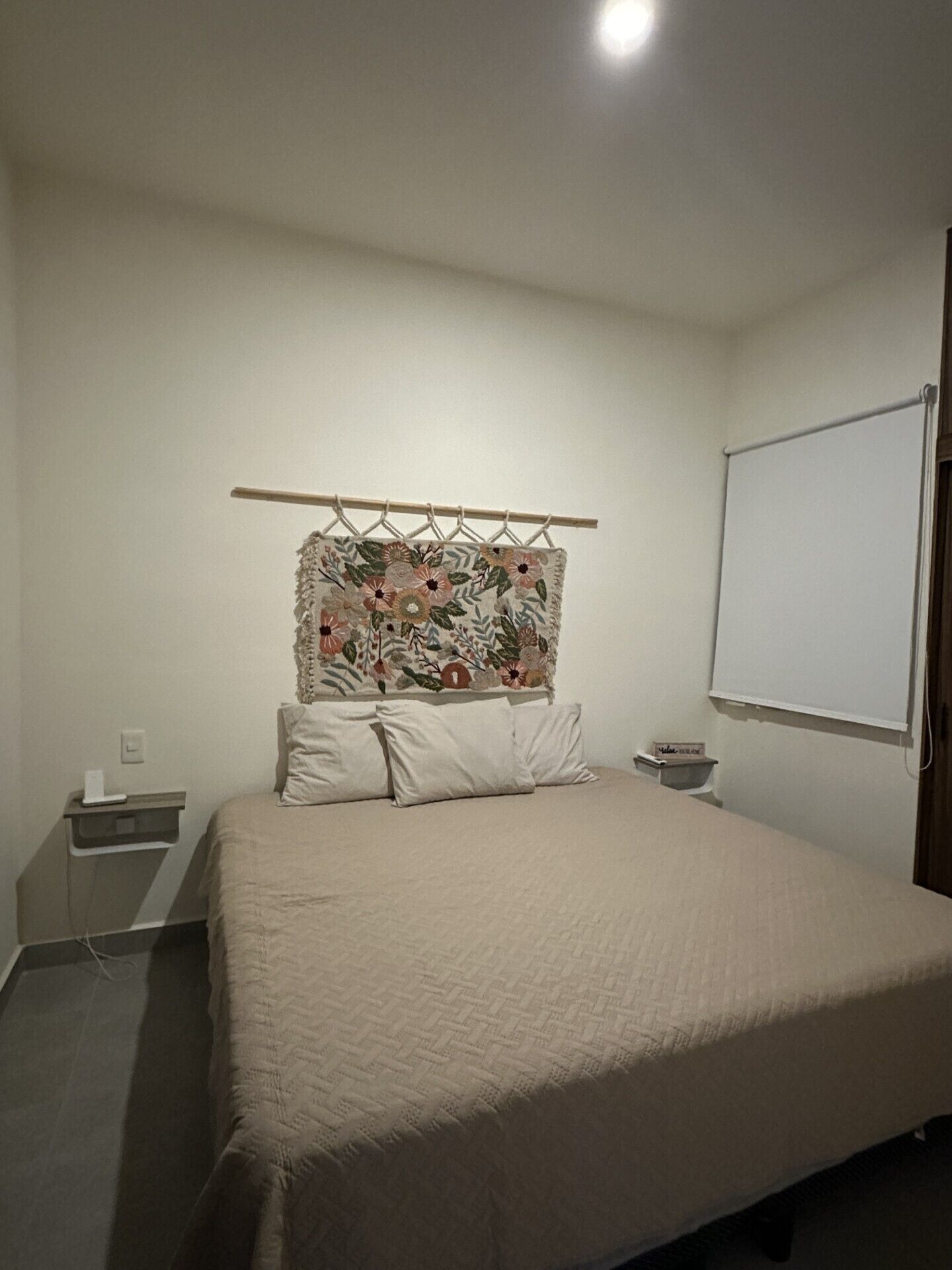 A bedroom with a bed, a nightstand, a wall-mounted TV, and a plain wall.