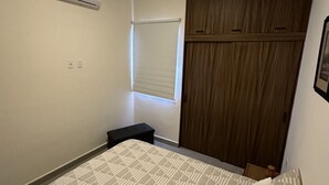 A bedroom with a bed, a wardrobe, a window with blinds, an air conditioning unit, and a small table. - Araquuna gated community, 2 bd condo close to PV, Sayulita, Bucerias (Mezcales)