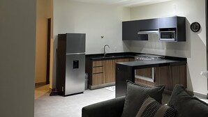 A modern kitchen with a built-in stove, microwave, and refrigerator. There is a dark-colored sofa with patterned cushions in the foreground. - Araquuna gated community, 2 bd condo close to PV, Sayulita, Bucerias (Mezcales)