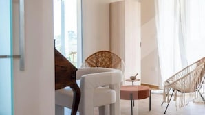 A modern room with a white chair, a wicker chair, a small table, and a tall white cabinet.
