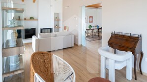 A modern living room with a sofa, a glass cabinet, a wooden chair, a white armchair, and a wooden desk.