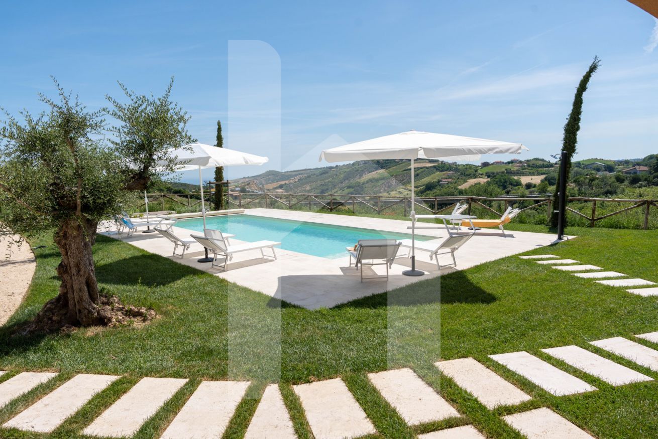 A swimming pool with lounge chairs and umbrellas, surrounded by a grassy area and stone steps.