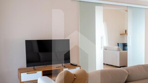 A modern living room with a flat-screen TV, a sofa, and a sliding glass door leading to another room.