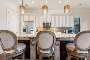 A kitchen with white cabinets, a stainless steel refrigerator, a microwave, and a large island with three chairs. - 🌊Tees & Tides | 2 Golf Carts | Golf Course Views | FREE Golf ⛳ (Miramar Beach)