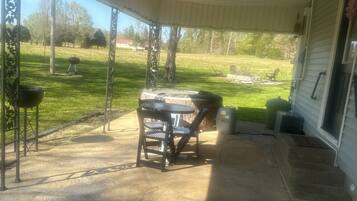 A covered patio with a table and chairs, a barbecue grill, and a view of a grassy yard.