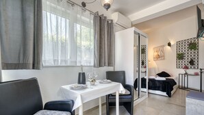 Ein modernes Hotelzimmer mit Essbereich, einem Bett mit schwarzer Bettdecke, einem kleinen Tisch mit weißem Tischtuch und einem Stuhl.