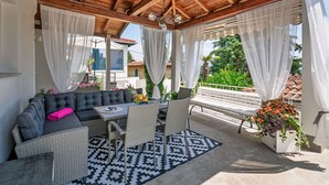 Eine Terrasse im Freien mit Holzboden, Korbmöbeln und einem gemusterten Teppich.
