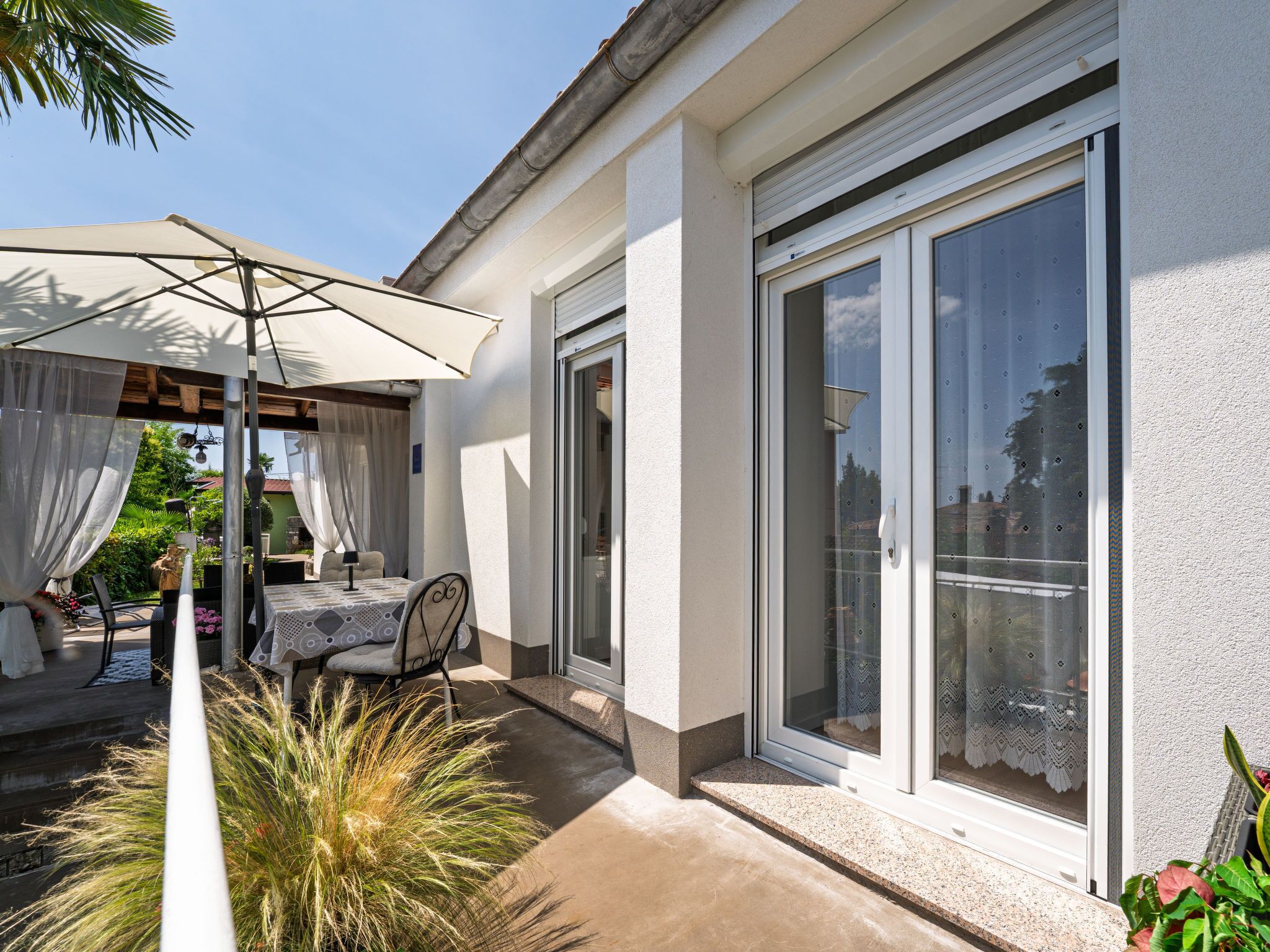 Une terrasse avec une table et des chaises, un espace couvert avec un parasol et une porte-fenêtre coulissante.
