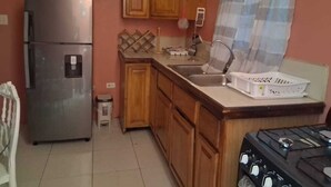 Cocina compacta con refrigerador, estufa, alacenas de madera y una ventana con cortinas.