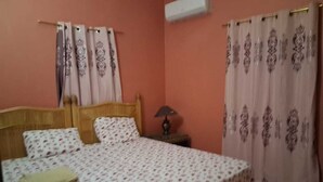 Un dormitorio con cama, cortinas, mesita de noche y lámpara.