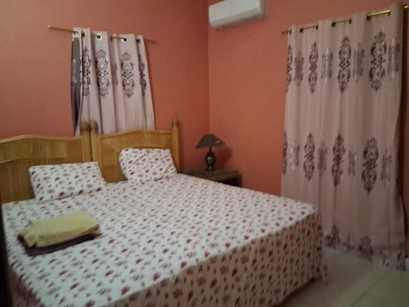 Un dormitorio con cama, cortinas, mesita de noche y lámpara.