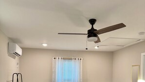 A bedroom with a bed, a ceiling fan, an air conditioner, a window with curtains, bedside tables, and a mirror.