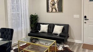 A living room with a black sofa, a glass coffee table, a cowhide rug, and a painting on the wall.
