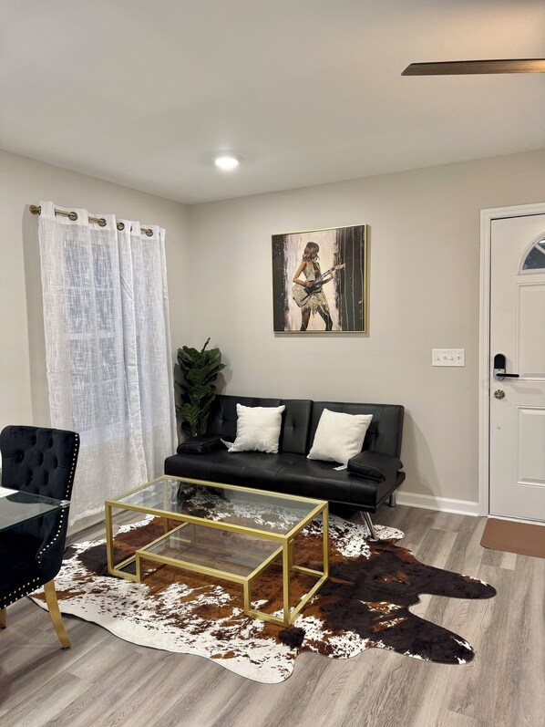 A living room with a black sofa, a glass coffee table, a cowhide rug, and a painting on the wall.