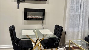 A modern dining area with a glass table, black upholstered chairs, and a flat-screen TV above.