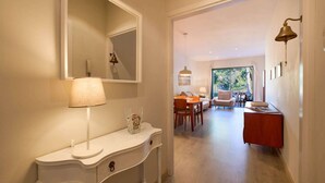 Un couloir avec une console blanche, un miroir et une lampe. On aperçoit à l’arrière-plan un coin repas avec une table et des chaises.