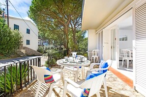 A patio with outdoor seating, a table with dishes, and a view of a white building and trees.
