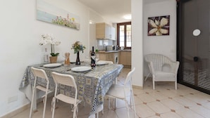 A dining area with a table set for four, chairs, a kitchen in the background, and a door with a flower painting. - Parque Santiago II - 2 Bed Sea View (Playa de Las Americas)