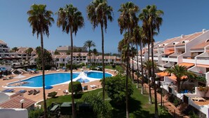 A hotel with a swimming pool, palm trees, and multiple balconies. - Parque Santiago II - 2 Bed Sea View (Playa de Las Americas)