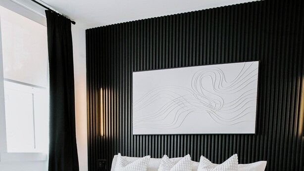 Ein modernes Schlafzimmer mit einem großen Bett, einem bequemen Sessel und einem großformatigen, abstrakten Kunstwerk an der Wand.