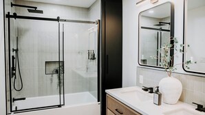 A modern bathroom with a glass-enclosed shower, a white sink, a large mirror, and a vase with a plant. - M2 - Double Queen room #4 (Dalhousie)