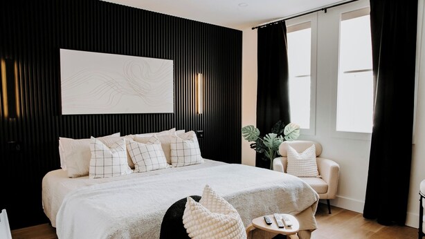 A modern bedroom with a large bed, a side table, a chair, and a large window with curtains. - M2 - Family room # 2 (lower level) (Dalhousie)