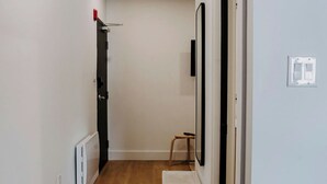 A hallway with wooden flooring, a radiator, a white shelf, and a door with a black frame. - M2 - Family room # 2 (lower level) (Dalhousie)