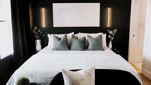 A modern bedroom with a large bed, black and white decor, and a wall-mounted abstract art piece.