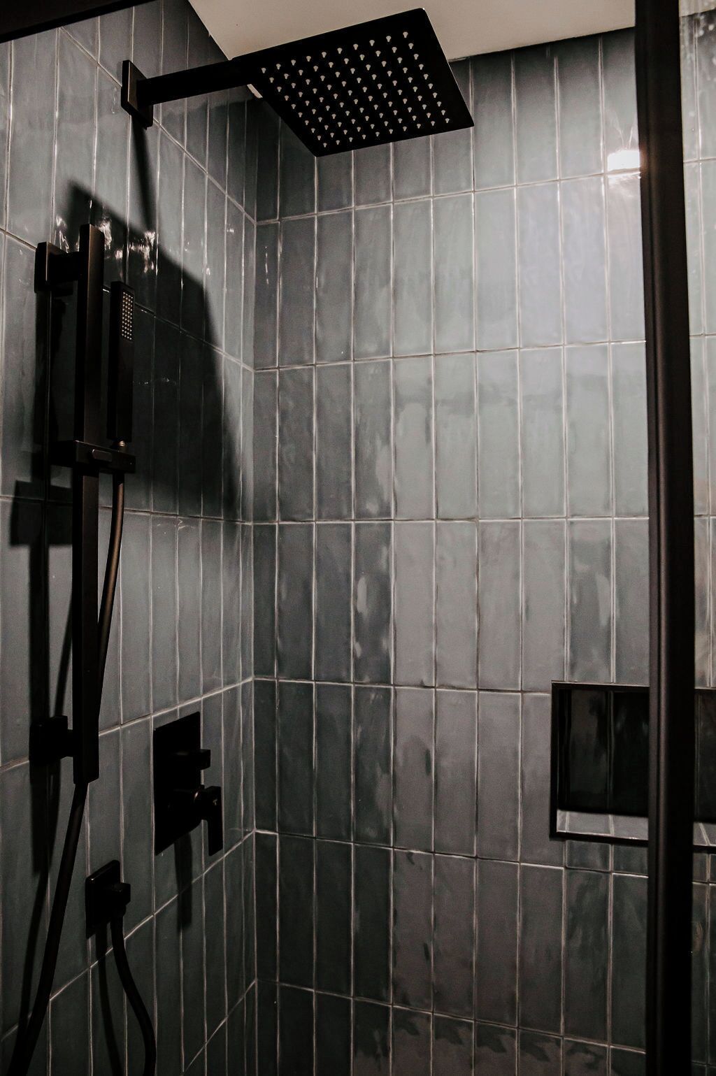 A shower area with a black rain showerhead and a handheld showerhead mounted on the wall.