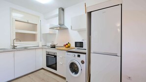 Ett modernt kök med vita skåp, en inbyggd ugn, en mikrovågsugn, en tvättmaskin och ett kylskåp.