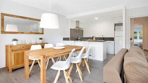 Une cuisine moderne avec une table à manger en bois et des chaises blanches, un grand miroir et un luminaire suspendu.