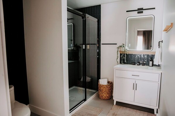 A modern bathroom with a glass shower enclosure, a white vanity with a mirror, and a wicker basket.