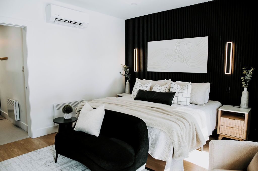 A modern bedroom with a black accent wall, a large bed with white bedding, a black chair, and a bedside table with a vase.