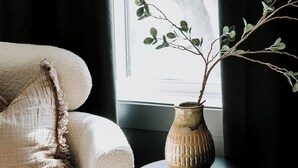 A cozy room with a plush armchair, a small round black side table, and a vase with a branch. - M2 - Spacious King Room # 3 (Dalhousie)