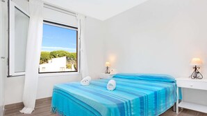Une chambre à coucher avec un lit, deux tables de chevet, une fenêtre avec des rideaux et une vue sur la verdure à l’extérieur.