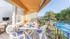 Un balcon donnant sur la piscine, avec des chaises blanches, une table sur laquelle est posé un journal et un téléviseur sur un meuble.